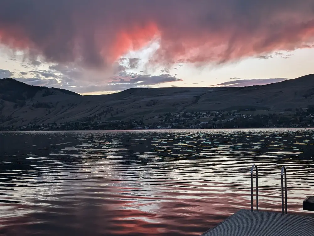 Pink storm clouds over Okanagan Lake and the far hillside, seen from a swim dock, June 21, 2026, 9:20 p.m.