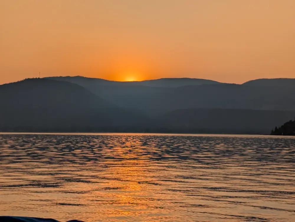 Orange sun setting behind the hills across Okanagan Lake from Okanagan Landing, September 3, 2025, 7:07 p.m.